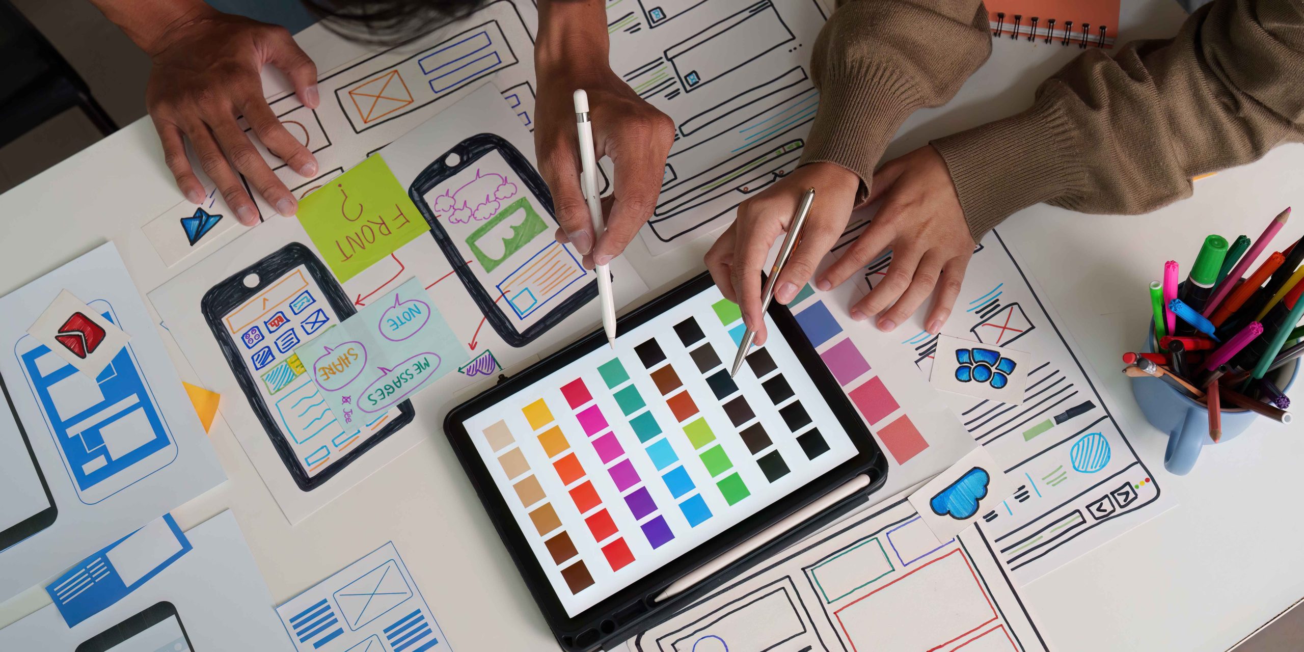 Designers focus on selecting colors and refining wireframes, showcasing the detailed work in UI/UX design.